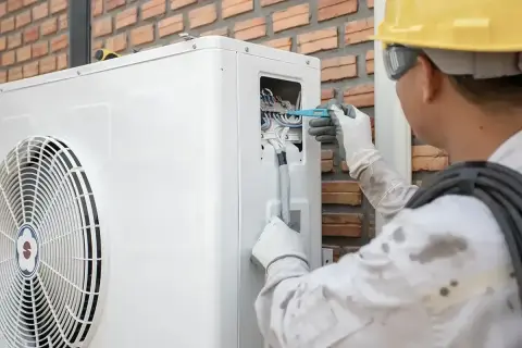Technik w żółtym kasku reguluje okablowanie pompy ciepła, co może pomóc w optymalizacji jej pracy, np. jak zmniejszyć taktowanie pompy ciepła.