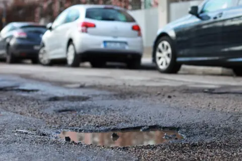 Poprzeczna nierówność jezdni z kałużami i zaparkowanymi samochodami.