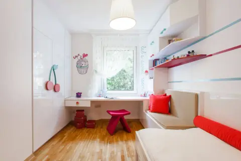 Ein heller Schreibtisch vor dem Fenster in einem Kinderzimmer, mit bunten Akzenten und Spielzeug.