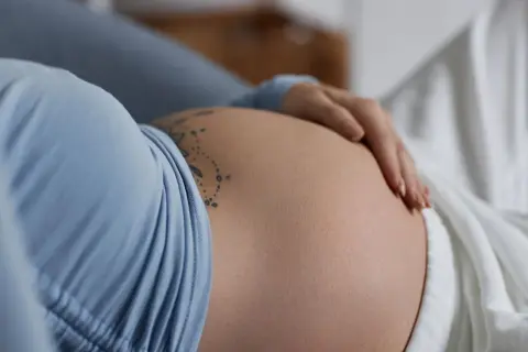 Dłoń spoczywa na zaokrąglonym, twardym brzuchu z tatuażem.