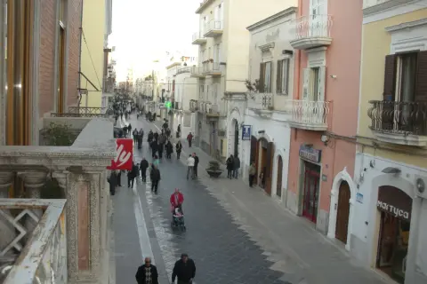 Passeggiata serale per gli abitanti di Manfredonia in una via commerciale animata, con negozi e palazzi storici.