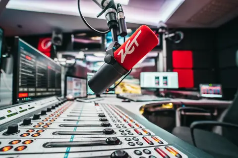 Mikrofon radiowy z logo ZET na tle konsolety i monitorów w studiu.