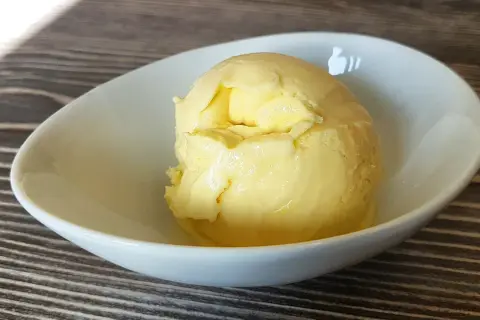 Cremiges Mango-Eis, selbst gemacht mit der Eismaschine, in einer weißen Schale auf Holztisch.