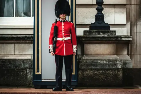 Un guardia con uniforme rojo y sombrero de piel, un típico inglés, vigila la entrada de un edificio histórico.