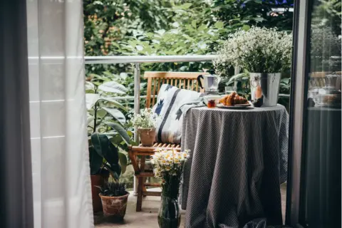 Gemütlich einen kleinen Balkon gestalten: Frühstück mit Kaffee, Croissant und Blumen auf dem Tisch.