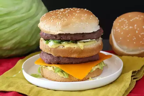 Domowy Big Mac z dwoma kotletami, serem, sałatą i sosem na talerzu.