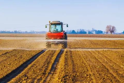 Czerwony traktor rozsiewa wapno z magnezem na polu, przygotowując ziemię do nowego sezonu.