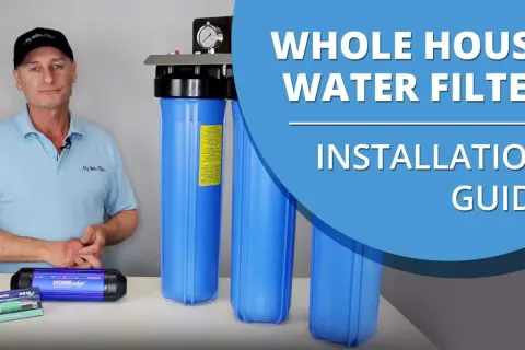 Man in a cap and polo shirt stands next to a whole house water filter system, ready for installation.