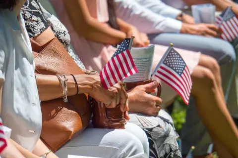 Manos sostienen pequeñas banderas de EE.UU. en un evento, quizás celebrando el sueño de estudiar en Estados Unidos siendo español.