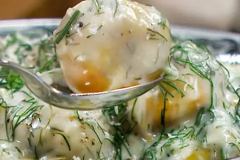 En sked lyfter upp en bit krämig dillstuvad potatis, täckt av färsk dill och en len sås.