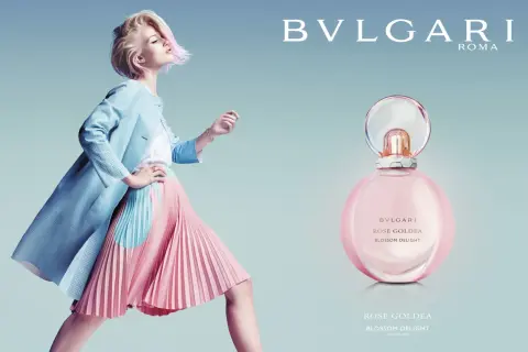 Kobieta w pastelowej stylizacji obok flakonu perfum Bvlgari Rose Goldea Blossom Delight.