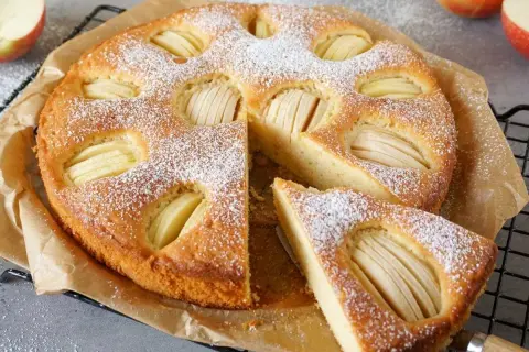Omas weltbester Apfelkuchen, mit Puderzucker bestäubt und saftigen Apfelscheiben, wartet darauf, genossen zu werden.