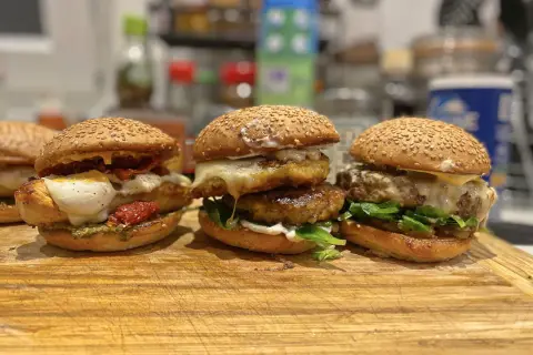 Trois burgers gras appétissants, garnis de fromage fondant, légumes frais et tomates séchées, prêts à être dégustés.