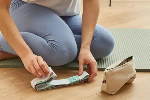 Kobieta w legginsach przygotowuje pasek do jogi na macie. Obok leży woreczek.