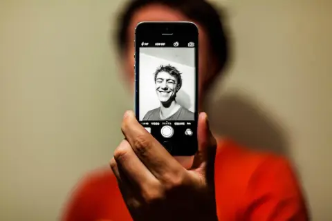 En person tar en selfie med en iPhone. Personen ler brett mot kameran.