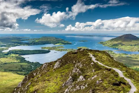 Vue panoramique du lac du Connemara, un lieu d'une beauté sauvage avec des montagnes verdoyantes et des eaux bleues scintillantes sous un ciel nuageux.
