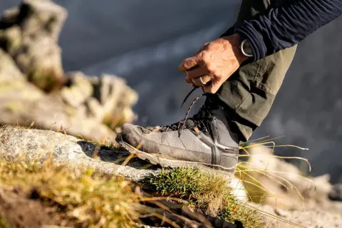 Mężczyzna sznuruje buty trekkingowe na kamieniu. Czy buty trekkingowe powinny być większe? Odpowiedź tkwi w komforcie i ochronie palców.