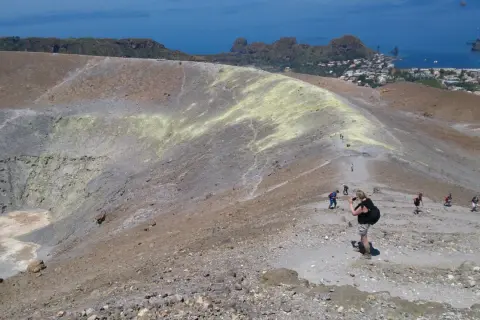 Une randonnée en Sicile sur un volcan actif, avec des sentiers rocailleux et une vue sur la mer et un village.