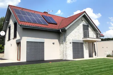 Nowoczesny dom z panelami solarnymi na dachu, otoczony zielonym ogrodem.