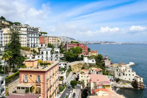 Färgstarka hus klättrar uppför sluttningen vid Neapel, Italien, med havet glittrande i bakgrunden.