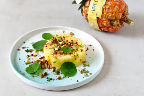 Okrągły kawałek ananasa, posypany pistacjami i przyprawami, na talerzu z liśćmi nasturcji. Czy mrożony ananas nadaje się do galaretki?