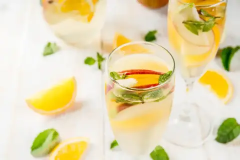 Verre de sangria blanche garni de tranches de pomme, d'orange et de menthe fraîche. Parfait pour une journée ensoleillée.