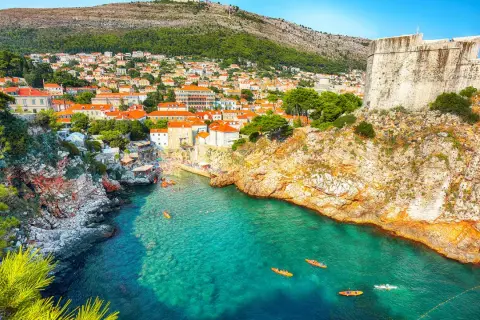 Kajaker på tur i det turkosa vattnet vid Gamla stan Dubrovnik, med klippor och stadens takåsar i bakgrunden.