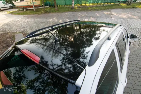 Błyszczące oklejenie dachu samochodu odbija drzewa i słońce. Eleganckie wykończenie dodaje autu stylu.