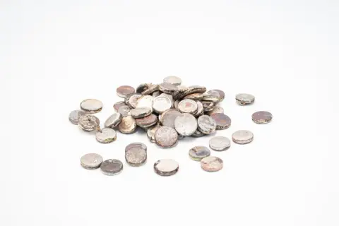 Kupa okrągłych, metalowych elementów, wyglądających jak zużyte baterie lub kapsle, stanowiąca złom srebra.