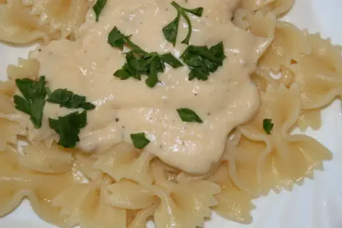 Pyszny makaron farfalle z kremowym sosem serowym, udekorowany świeżą natką pietruszki. Idealny na szybki obiad.