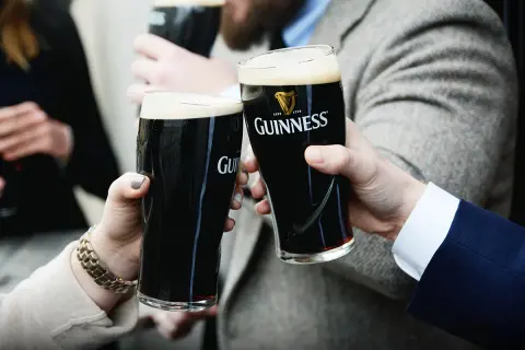 Dwie osoby wznoszą toast szklankami ciemnego piwa Guinness. To klasyczne piwo ma ok. 4,2% alkoholu.