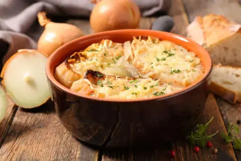 Un bol de soupe à l'oignon gratinée, prêt à être dégusté. Une recette réconfortante avec du pain et du fromage fondu.