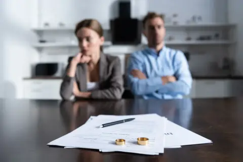 Para rozwiedzionych siedzi przy stole z dokumentami rozwodowymi i obrączkami.