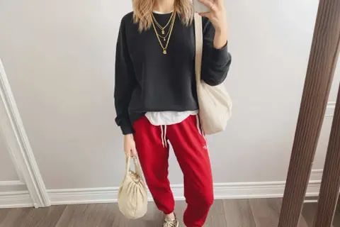 Styling-Idee: Schwarzer Pullover, weiße Schicht, rote Hose mit weißen Streifen, Leo-Sneaker und cremefarbene Taschen. Perfekt, wenn du fragst, was passt zu roter Hose!