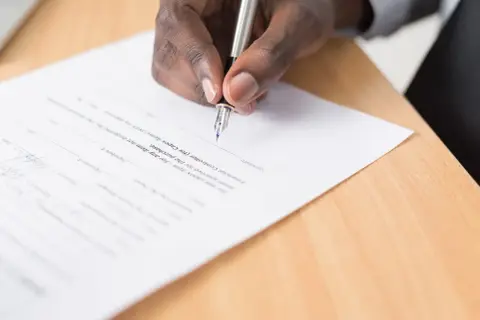 Dłoń podpisuje dokument piórem. To ważny krok, który może być częścią nauki angielskiego na poziomie B2, np. przy podpisywaniu umowy o pracę.