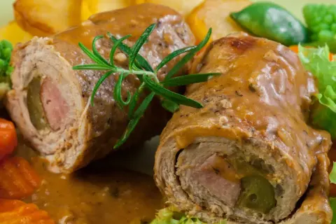 Dwa soczyste zrazy wieprzowe w sosie, podane z pieczonymi ziemniakami i warzywami.