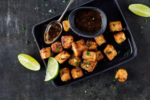 Tofu in padella dorato e croccante, servito con salsa e spicchi di lime.