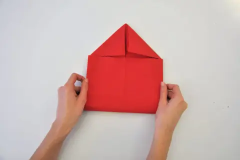 Mains tenant une feuille rouge pour un pliage serviette enveloppe. Le papier est plié en forme de maison.