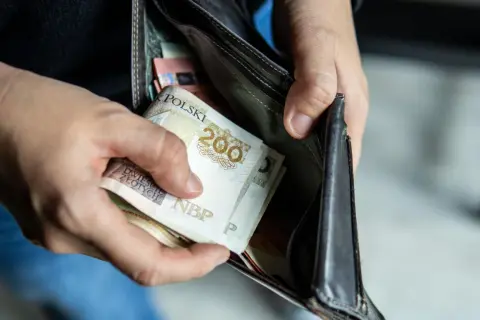 Ręce wkładają polskie banknoty do portfela. Czy to wystarczy na pensję minimalną 2026?