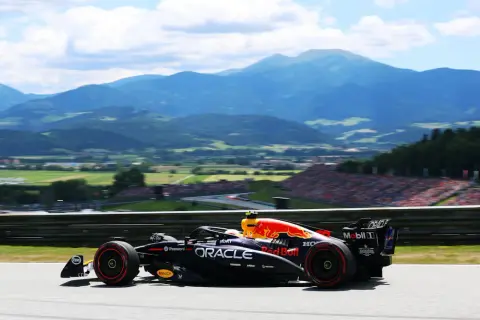 Un coche de Red Bull compite en el Gran Premio de Austria, con montañas y público al fondo.