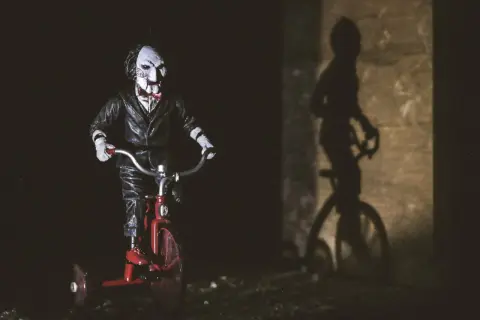 Lalka Billy z Piły na czerwonym trójkołowcu, cień na ścianie. Idealne do listy horrorów.