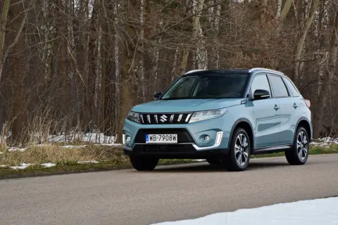 Jasnoniebieska Suzuki Vitara na drodze leśnej, z drzewami w tle i resztkami śniegu.