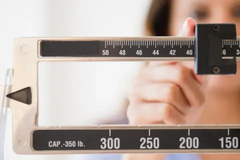Bilancia meccanica con una mano che regola il peso. La scala mostra numeri come 50, 48, 46, 44, 42, 40, 36, 34, 32, 300, 250, 200, 150. Forse la persona sta pensando che le more fanno ingrassare.
