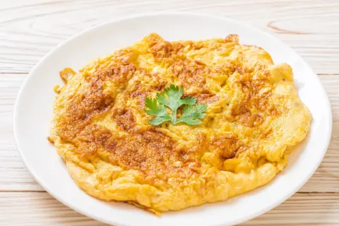 Złocisty omlet na talerzu, idealny jako omlet dla niemowlaka. Delikatny, puszysty, z gałązką pietruszki.