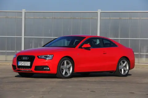 Czerwone Audi S5 z 2014 roku, sportowe coupe z elegancką linią, zaparkowane przed nowoczesnym budynkiem.