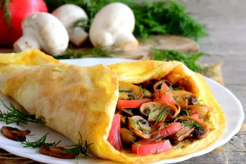 Puszysty omlet z pieczarkami i pomidorami, udekorowany koperkiem. Idealny na śniadanie.