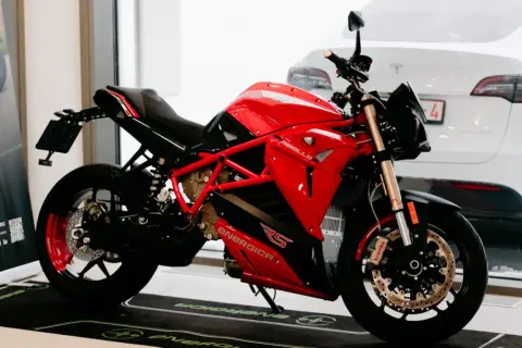 Motocicleta roja y negra Energica RS, lista para la acción. Detrás, un coche blanco.