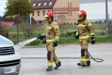 Strażacy w akcji, jeden z węża wodnego. Zastanawiasz się, ile zarabia strażak? To praca pełna poświęcenia.