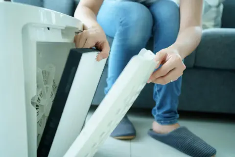 Osoba wymienia filtr w oczyszczaczu powietrza. Czy filtr HEPA można myć wodą? Zazwyczaj nie, ale warto sprawdzić instrukcję.