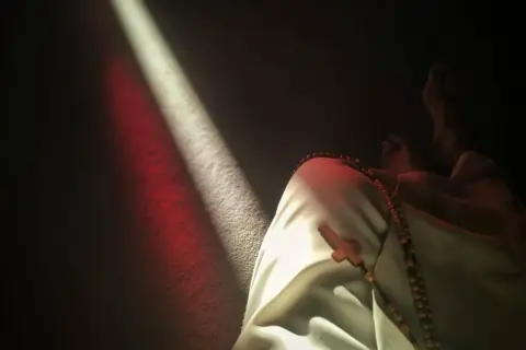 Światło pada na postać w białej szacie z różańcem. Czy to kościół Boga Wszechmogącego, czy sekta?